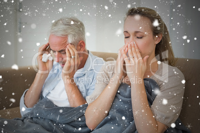 Composite image of sick couple sitting on the couch under a blan