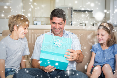 Composite image of father opening gift given by children on sofa