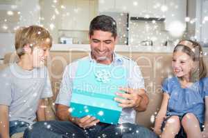 Composite image of father opening gift given by children on sofa