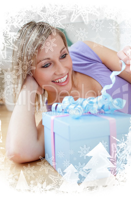 Cheerful blond woman holding a present lying on the floor