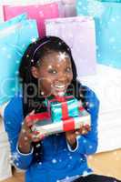 Composite image of cheerful woman holding a present sitting on t