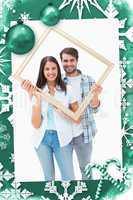 Composite image of happy young couple holding picture frame