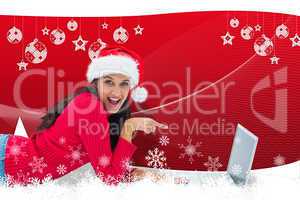 Composite image of festive brunette pointing at laptop