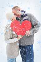 Composite image of happy mature couple in winter clothes holding red heart