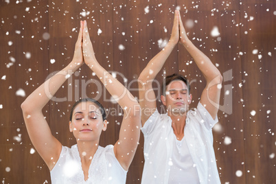 Peaceful couple in white doing yoga together with hands raised
