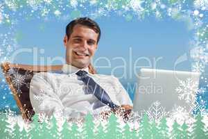 Cheerful young businessman lying on a deck chair with his comput