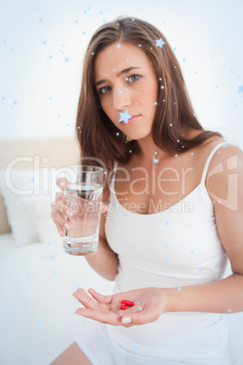 Woman with pills in one hand and a glass of water in the other looking worried