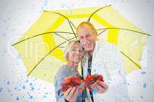 Happy mature couple showing autumn leaves under umbrella