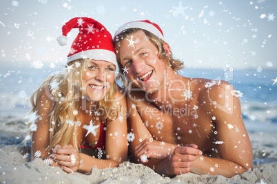 Composite image of couple lying on beach wearing christmas hats