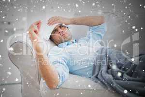 Composite image of sick man lying on sofa checking his temperatu