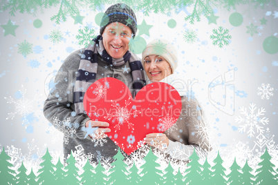 Happy mature couple in winter clothes holding red heart