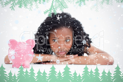 Young woman lying down resting her head on her hands is looking at a piggy bank