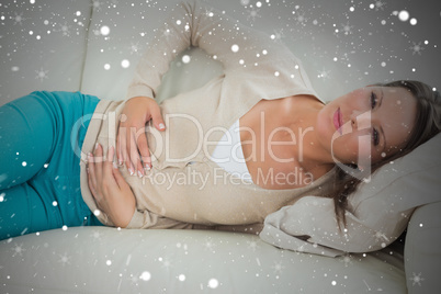Composite image of woman lying on the sofa with upset stomach