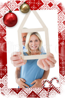 Composite image of happy couple holding house outline