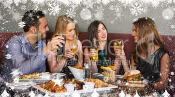 Composite image of happy friends sitting together having dinner