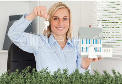 Gorgeous businesswoman presenting model house and keys looks int