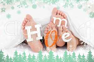 Composite image of pair of feet under duvet with home text