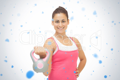 Cheerful sporty brunette holding grey and pink kettlebell