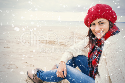 Smiling woman in stylish warm clothing sitting on beach