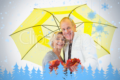 Happy mature couple showing autumn leaves under umbrella