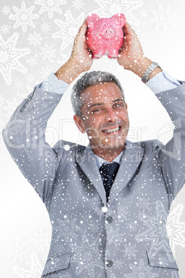 Composite image of cheerful businessman holding piggy bank above