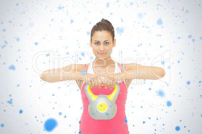 Smiling sporty brunette holding grey and yellow kettlebell