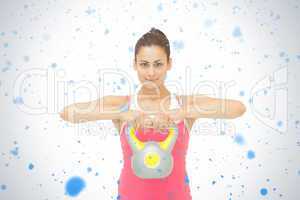 Smiling sporty brunette holding grey and yellow kettlebell