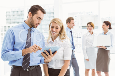 Business couple using digital tablet with colleagues behind