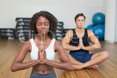 Fit couple sitting in lotus pose in fitness studio