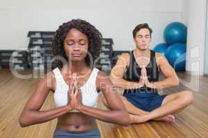 Fit couple sitting in lotus pose in fitness studio