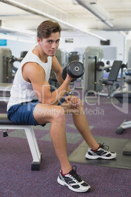 Fit man lifting dumbbells sitting on the bench