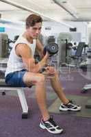 Fit man lifting dumbbells sitting on the bench
