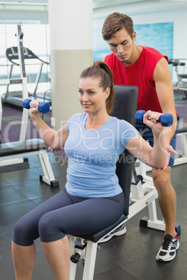 Personal trainer helping client lift dumbbells