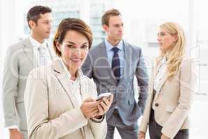 Businesswoman text messaging with colleagues in meeting behind