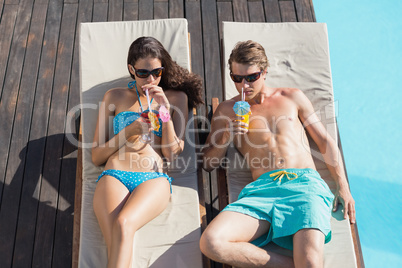 Couple with drinks on sun loungers by swimming pool
