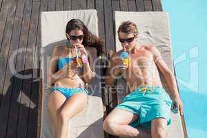 Couple with drinks on sun loungers by swimming pool