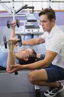 Personal trainer helping client lift dumbbells