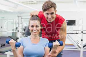 Personal trainer helping client lift dumbbells