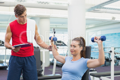 Personal trainer helping client lift dumbbells