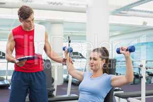 Personal trainer helping client lift dumbbells