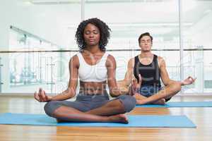 Fit couple sitting in lotus pose in fitness studio