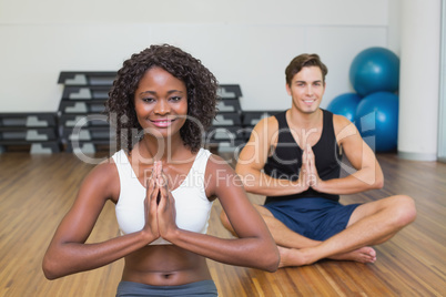 Fit couple sitting in lotus pose in fitness studio