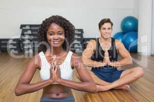 Fit couple sitting in lotus pose in fitness studio