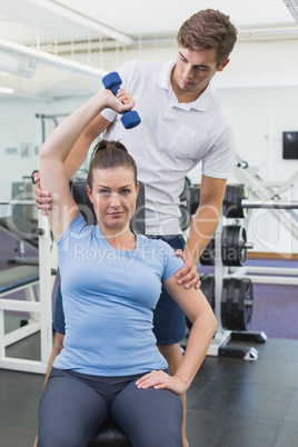 Personal trainer helping client lift dumbbell