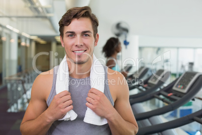 Handsome man smiling at camera beside treadmills