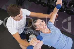 Personal trainer helping client lift dumbbells