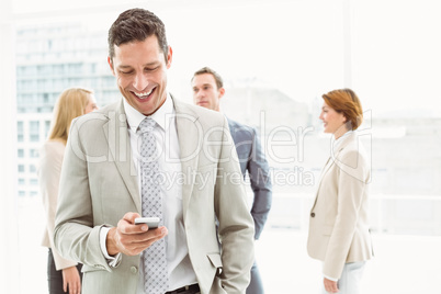 Businessman text messaging with colleagues in meeting behind