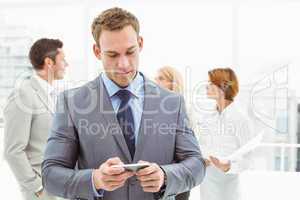 Businessman text messaging with colleagues in meeting behind