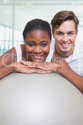 Personal trainer and client smiling at camera with exercise ball