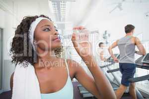 Fit woman drinking water beside treadmills